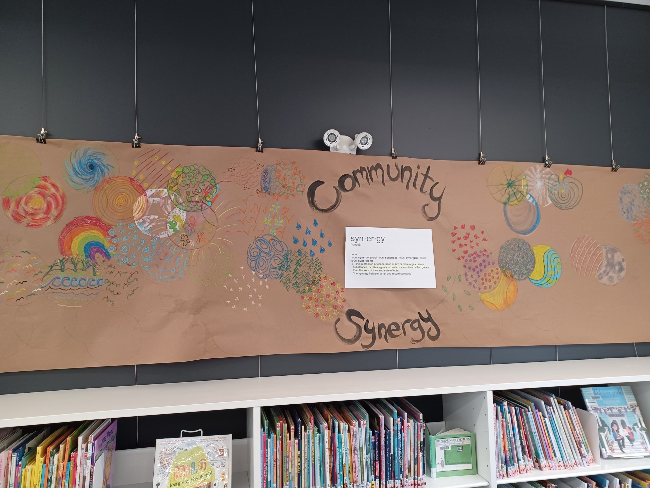 Community Synergy art project, brown art paper is hung in the Library, with colourful swirls of colour added by community members.