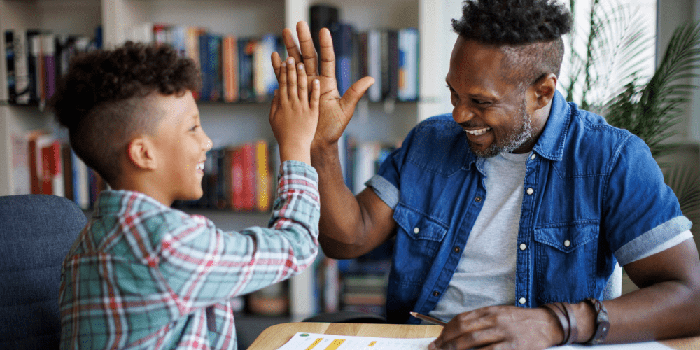 An adult and child sharing a high-five at a study table in a library.