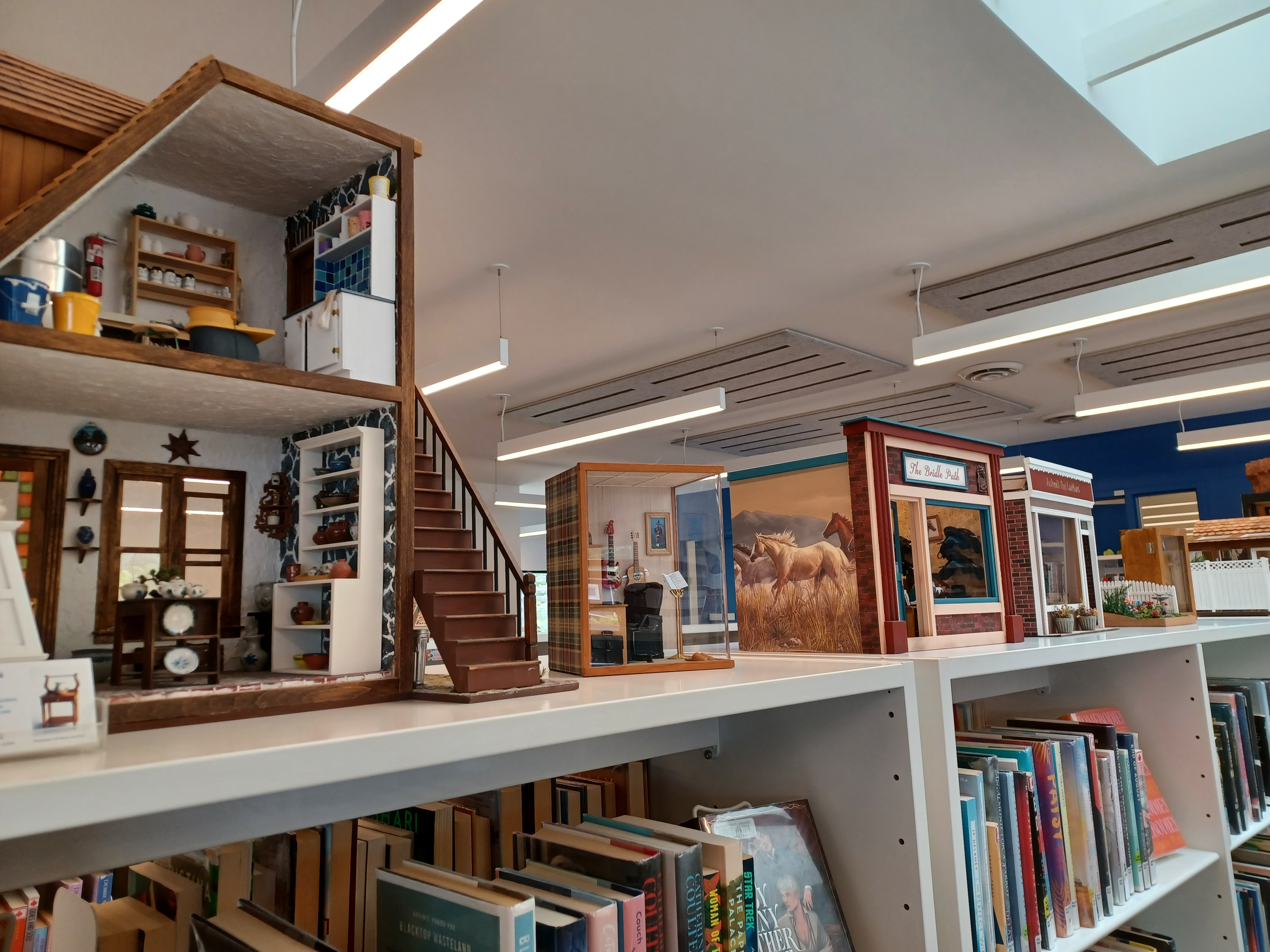 A series of miniature home / building displays, atop a Library book shelf.